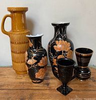 Lot of five vases arranged on a wooden surface, showing various styles and sizes including mustard yellow and black with gold accents.