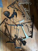 Top-down view of various metal brackets on wooden floor showing ornate shelf brackets, angular support brackets, and cast metal bracket.
