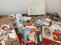 Wide view of vintage greeting cards and stationery laid out, showing various holiday cards featuring Santa Claus, poinsettias, and other seasonal imagery.
