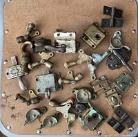 Top-down view of assortment of vintage hardware laid out on a wooden board, showing various latches, locks, handles, and hinges.