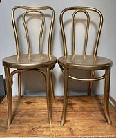 Two vintage gold painted bentwood chairs shown from front on wood floor.