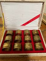 Boxed set of twelve brass napkin rings in original box with white fabric lined lid and red velvet base insert.