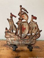 Front view of a vintage cast metal ship doorstop showing detailed sails, flags, and hull with aged paint and rust.