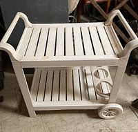 Front and side view of the white slatted vintage bar cart showing two-tier shelving and large side wheels.