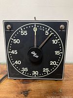 Front view of vintage photographic dark room timer showing black dial with white numbers, central knob labeled 'Berleb', and toggle switches on top corners.