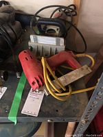 Arrow electric stapler and Freud biscuit joiner placed on shelf. Stapler red plastic with yellow power cord, biscuit joiner silver and gray with measurement guide.