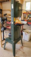 Front view of green Craftex band saw on four-leg stand, power cord hung on side, gooseneck light attached