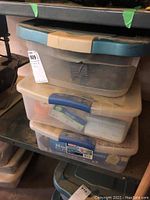 Three stacked plastic bins with blue and beige lids containing tools and accessories