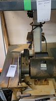 Side view showing the belt sander assembly and black motor housing mounted on a white metal stand.