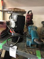 Photo of Craftsman electric sander in black and silver with a black handle alongside a red Toolshop laminate trimmer and teal-blue Makita sander, all resting on a shelf.