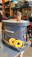 Overall frontal view of the Mastercraft spindle sander showing sanding drum and yellow sanding accessories on the base.