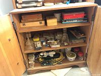 Wooden cabinet open showing three shelves with hardware and accessories