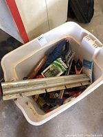 White bin containing assorted tools including multiple metal clamps, a metal folding ruler, and the Energizer battery charger in packaging.