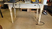 Front view of vintage workshop table showing painted turned legs and lower apron