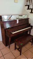 Photo of antique upright piano with matching bench, showing front and left side views.