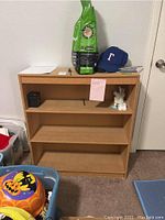 Front view of the particle board bookcase showing three shelves and some small objects placed on it.
