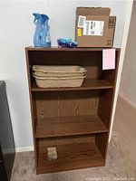 Front view of composite laminate bookcase showing four shelf levels with some items placed but not included in lot.