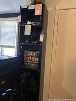 Full view of the narrow black bookcase, containing various items but contents not included in sale.