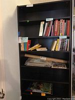 Full front view of the black IKEA bookcase partially filled with books, documents, and a tube, showing adjustable shelves.
