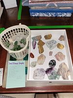 Photo showing mineral sample stones arranged in a tray and a white basket holding several small polished stones next to a list of mineral names written on a note.