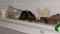 Full view of the lot on a white mantel including geodes, petrified wood, Texas-shaped stone, rough rocks in plastic bags, and small cups.