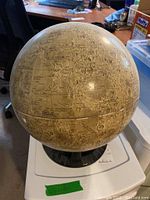 Photo of vintage beige-toned moon globe circa 1970 with detailed lunar markings including labeled seas and craters on a black circular plastic stand