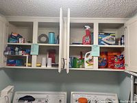 Wide view of kitchen cabinet shelves showing various brands of home care and cleaning products including Ziploc bags, detergents, iron, and cleaning sprays.