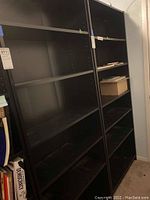 Photo of full view of two adjacent black IKEA bookcases with empty adjustable shelves