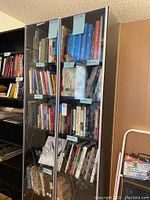 Front view of dark-colored IKEA bookcase filled with books behind glass doors, showcasing adjustable shelves.