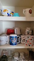 Shelf with additional mugs of varying colors and styles along with glass mugs and cups below