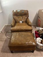 Full view of the vintage brown leather chair and matching ottoman on carpeted floor, showing wear and included care kit.