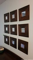 Nine square mirrors arranged in a 3x3 grid on the wall, each with dark wood frames and small centered mirrors.