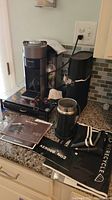 Full view of Nespresso Vertuo coffee machine, Aeroccino3 frother, coffee pod disposal unit, manuals, and coffee pods on kitchen counter.