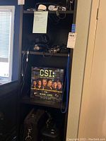 Photo of shelving with electronics and copy of CSI board game, showing lot context and contents