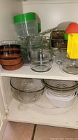 Shelves with clear and brown glass baking and mixing bowls, plastic salad spinner with green lid, and yellow cookie cutters