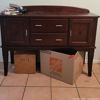 Front view of the wooden sideboard showing two side cabinets, two center drawers with silver handles, tapered legs, and wood surface with visible wear.
