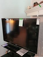 Front view of a large Samsung flat-screen TV on a TV stand, black bezel, with a note attached and an owner's manual placed beneath the screen.
