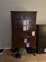 Full view of vintage dark wood highboy dresser with drawers, showing some scratches and scuffs. Shoes and clothes are placed in front for scale.