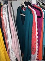 Photo of various women's long sleeve tops and sweaters hanging on hangers. Colors visible include yellow, pink, teal, coral with floral print, white with stripes, orange, red and white stripes, purple, turquoise.