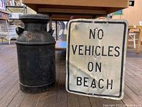 Full view of antique milk can and metal sign side by side on wooden floor under table