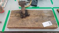 Side view of rusted vintage vise grip mounted on weathered wooden plank surrounded by other items on a table.