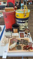 Wide view of lot showing red and pretzel tins, black/orange tin, miniature houses, cast iron sheep, trivet, and other antiques on tray and table.