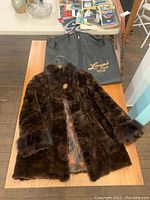 Full view of the dark brown blue fox fur coat laid flat on wooden surface with Lanzi Furs garment bag beside it.