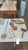 Photo showing eight folk craft items on a table including Russian nesting dolls, wooden bellows, brass ladle, lacquer boxes, miniature decor, gavel, and an Egyptian tile.