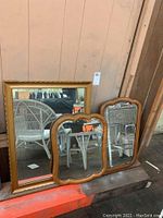 Three wooden framed mirrors; a large gold rectangular mirror and two smaller matching natural wooden framed mirrors with curved edges forming a pair.