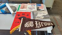 Overview of lot on table including Brown University pennant, R.H.S. 1985 banner, folded American flag, and four publications.