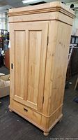 Front left angle view of pine wood pantry cabinet showing door, drawer, and top molding details.