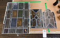 Photo of all three salvaged stained glass panels laying flat on a cardboard surface showing relative sizes and lead framing.