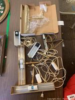 Five brass and glass showcase display lamps, one still in original box with plastic wrap, cords and switches visible on table.