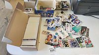 Wide shot featuring a cardboard box full of trading cards and multiple loose trading cards spread on a table surface.